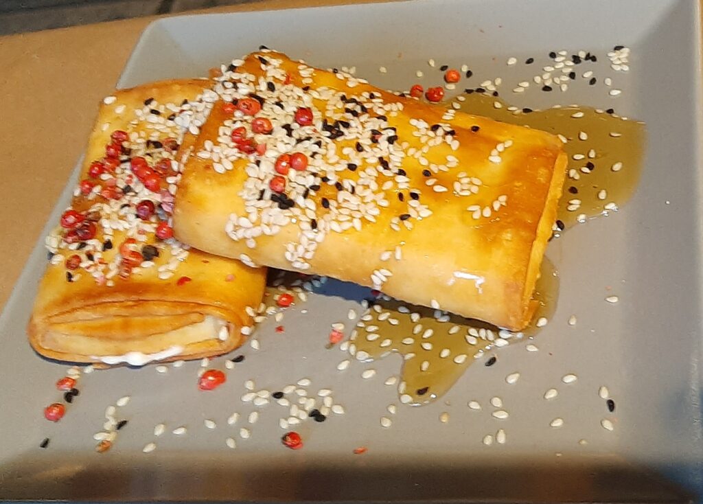 Two pieces of feta rolled in phylo and baked, garnished with colorful peppercorns and Greek honey