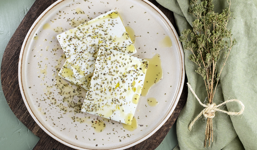 dish of sliced feta chees with oil and oregano, a bundl of dried thyme on a green napkin